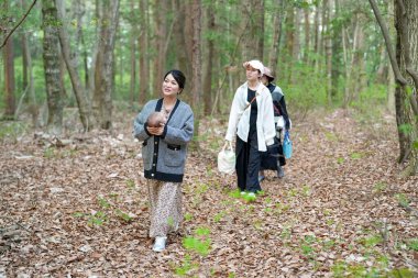 Kollarında küçük bir hayvanla ormanda yürüyen bir kadın. Diğer iki kadın onun arkasında yürüyor.