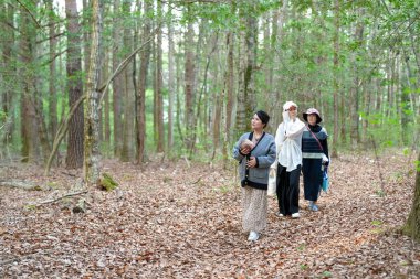 Bir grup kadın ormanda yürüyor, içlerinden biri bir bebek taşıyor. Manzara huzurlu ve huzurlu, kadınlar doğada vakit geçirmekten hoşlanıyor.