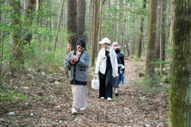 Bir grup kadın ormanda yürüyorlar, içlerinden biri bebek tutuyor. Manzara huzurlu ve huzurlu, kadınlar doğada vakit geçirmekten hoşlanıyor.
