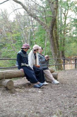 Ormandaki bir kütükte üç kadın oturuyor. İçlerinden biri bir bebek tutuyor.