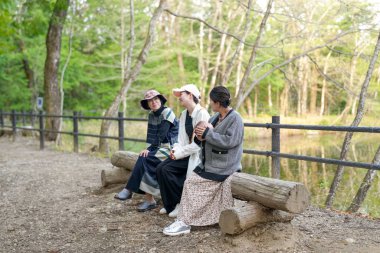 Parkta bir bankta oturan üç kadın. İçlerinden biri şapka takıyor. Manzara sakin ve huzurlu.