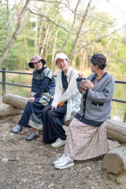 Ormanda bir kütüğün üzerinde oturan üç kadın. İçlerinden biri bir bebek tutuyor.