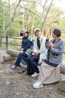 Ormanda bir kütüğün üzerinde oturan üç kadın. İçlerinden biri bir bebek tutuyor.