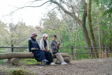 Ormandaki bir kütükte üç kadın oturuyor. İçlerinden biri bir bebek tutuyor.
