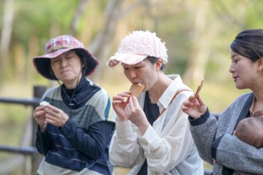 Üç kadın dışarıda yemek yiyor. Bir kadın pembe bir şapka takıyor. Sahne rahat ve rahat.