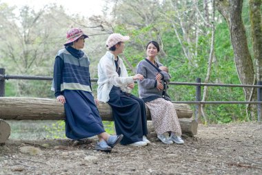 Ormanda bir kütüğün üzerinde oturan üç kadın. İçlerinden biri bir bebek tutuyor.