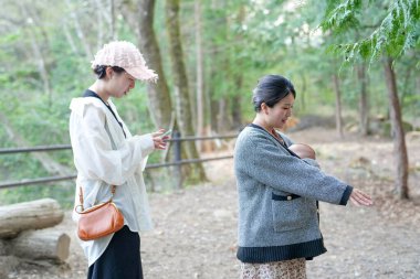 Bir kadın başka bir kadın izlerken bir bebeğin fotoğrafını çekiyor. Bebek siyah beyaz ceketli kadın tarafından tutuluyor.