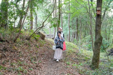 İki kadın ormanda bir patikada yürüyorlar. İçlerinden biri bir çanta taşıyor.