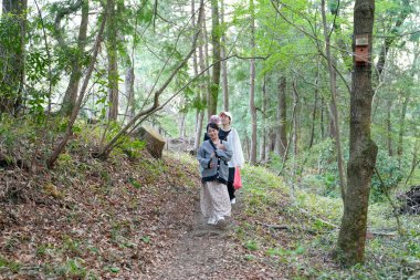 Bir kadın ormanda iki kadınla birlikte yürüyor. Kadınlar siyah beyaz giyiyorlar.