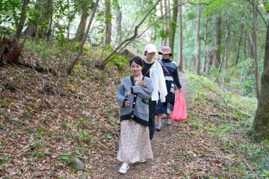 Bir grup kadın ormanda yürüyor, içlerinden biri bir çanta taşıyor. Manzara huzurlu ve huzurlu, kadınlar doğada vakit geçirmekten hoşlanıyor.