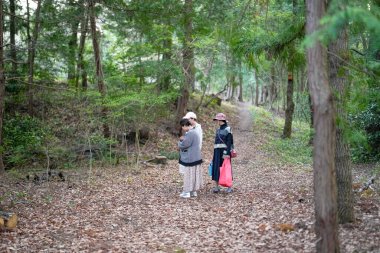 Bir ormanda üç kişi yürüyor. Bir tanesi kırmızı çanta takıyor.