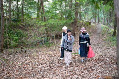 Üç kadın bir ormanda yürüyor, biri bebek taşıyor. Atmosfer sakin ve sakin. Arka planda öten kuşların sesleri var.