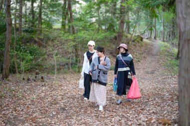 Bir ormanda bebekle yürüyen üç kadın. İçlerinden biri bir çanta taşıyor.