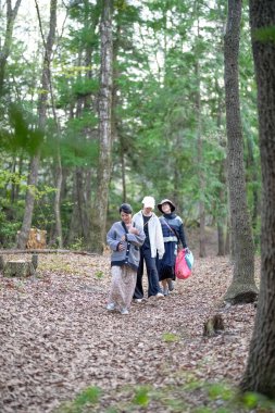 Üç kadın bir ormanda yürüyor, biri bir çanta taşıyor. Manzara huzurlu ve huzurlu, kadınlar doğada vakit geçirmekten hoşlanıyor.