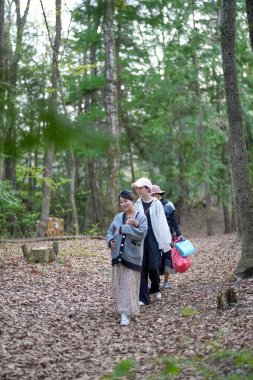 Bir grup insan, elinde bebek taşıyan bir kadınla ormanda yürüyorlar. Sahne huzurlu ve huzurlu, grup doğadaki zamanının tadını çıkarıyor.