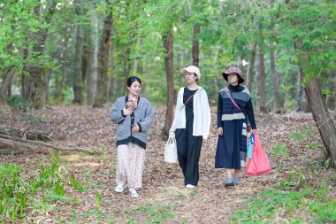 Üç kadın ormanda yürüyor, içlerinden biri bir bebek taşıyor. Manzara huzurlu ve huzurlu, kadınlar doğada vakit geçirmekten hoşlanıyor.