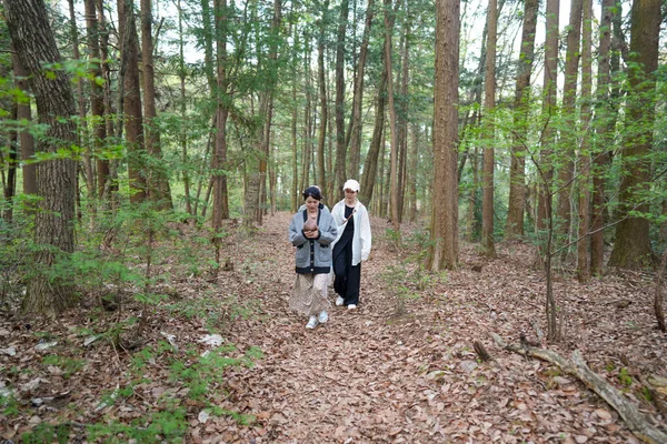 Ormanda yürüyen iki kadın, biri cep telefonu tutuyor. Manzara huzurlu ve sakin, kadınlar doğa tarafından çevrili ve sessiz bir yürüyüş yapıyorlar.