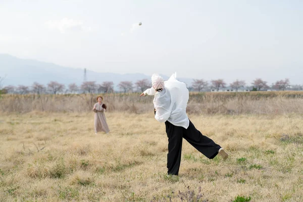 Beyaz elbiseli bir kadın tarlada topla oynuyor. Sahne huzurlu ve huzurlu, resimdeki tek nesneler kadın ve balo.