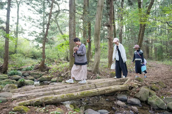 Bir grup insan bir ormandaki köprüden geçiyorlar. Kadınlardan biri bebek taşıyor.