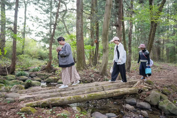 Bir grup kadın bir ormanda köprüden geçiyorlar. Kadınlardan biri bebek taşıyor.