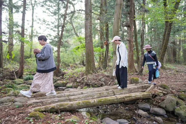 Bir grup insan ormandaki ahşap bir köprüden geçiyorlar. Kadınlardan biri bir bebek tutuyor.