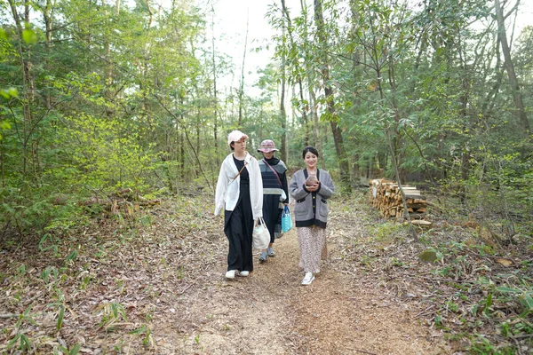 Üç kişi bir ormanda yürüyor, biri bir çanta tutuyor. Sahne huzurlu ve huzurlu, bir grup insan doğa yürüyüşünden zevk alıyor.