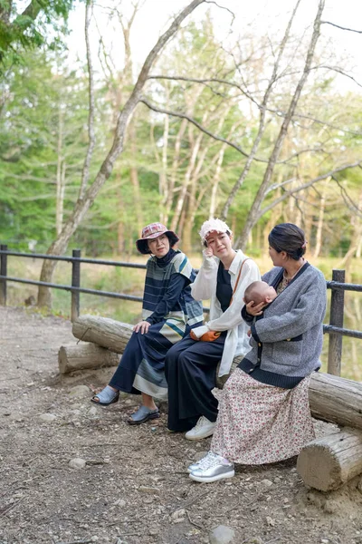 Ormanda bir kütüğün üzerinde oturan üç kadın. İçlerinden biri bir bebek tutuyor.