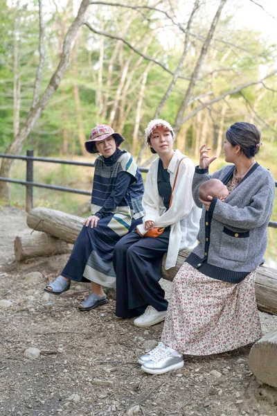 Ormanda bir kütüğün üzerinde oturan üç kadın. İçlerinden biri bir bebek tutuyor.