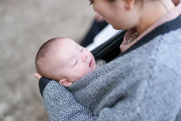Bir kadın uyuyan bir bebeği kollarında tutuyor. Bebek bir battaniyeye sarılmış ve çok memnun. Sıcaklık ve rahatlık kavramı, çünkü kadın güvenli bir yer sağlıyor.