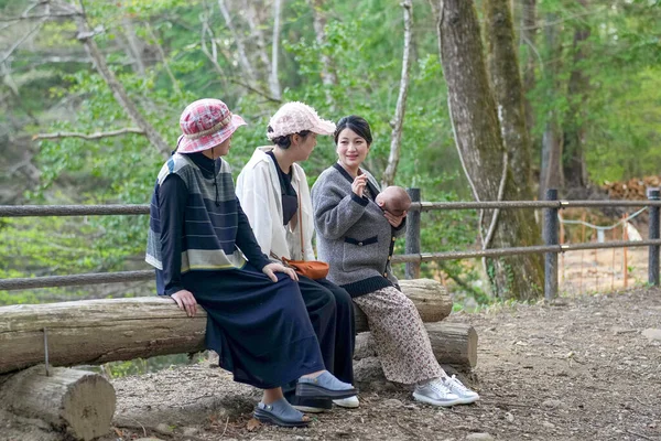 Üç kadın ormanda bir kütüğün üzerinde oturuyor, biri bebeği tutuyor. Manzara huzurlu ve huzurlu, çünkü kadınlar doğal ortamda birbirlerine eşlik etmekten hoşlanıyorlar.