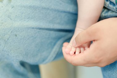 Bir bebeğin ayağı bir kişi tarafından tutuluyor. Bebek kot pantolon giyiyor. Bebeğin ayağı pembe ve beyaz bir beneği var.