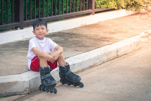Asiatischer Junge sitzt mit Rollschuhen auf dem Fußweg — Stockfoto