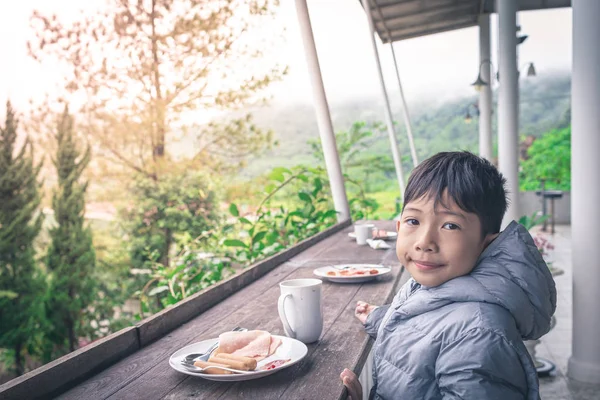 Lächelnd asiatisch junge ist eating breakfast auf ein schön natürlich bac — Stockfoto