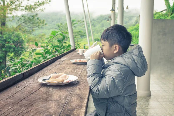 Asiatisches Kind im Kapuzenpullover hebt ein Glas, um Milch und Brühe zu trinken — Stockfoto