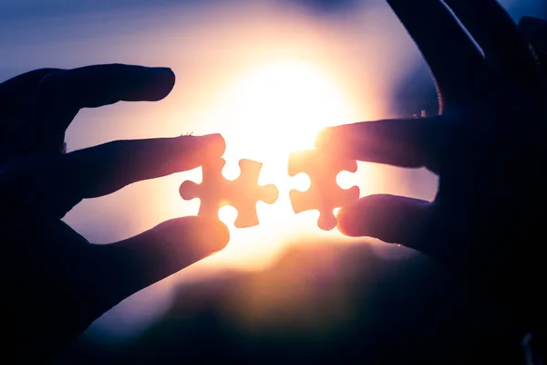 Dwie ręce trzymając puzzle na wieczornym świetle słońca — Zdjęcie stockowe