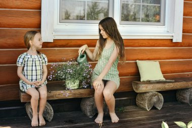 Açık havada birlikte eğleniyor ve dökme iki sevimli kız kardeş çiçekler üzerinde su 