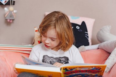 Evdeki kanepede kitap okuyan küçük çocuk.