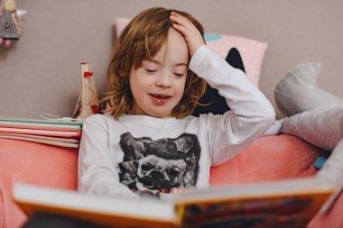 Evdeki kanepede kitap okuyan küçük çocuk.