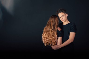 Stüdyoda siyah arka planda poz veren genç bir çift. 