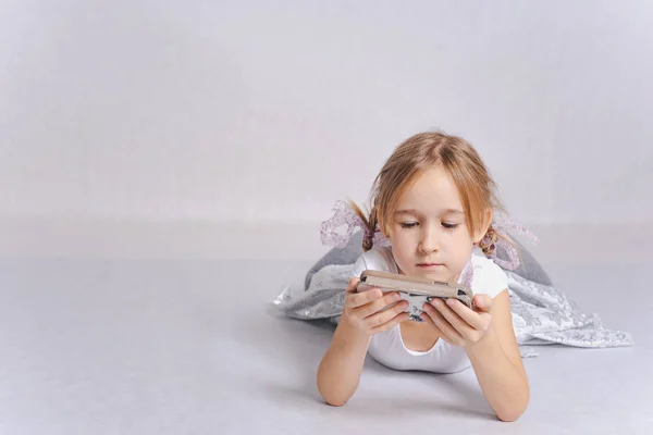 Linda Niña Mintiendo Jugando Teléfono Inteligente Sobre Fondo Gris —  Fotos de Stock