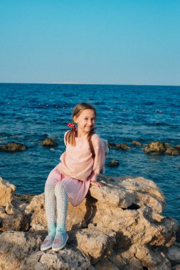 deniz arka planda kaya üzerinde oturan sevimli küçük kız 