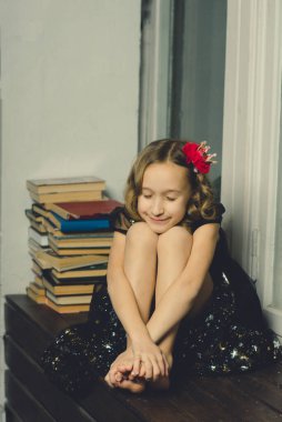 Küçük kız evde elinde kitaplarla poz veriyor.