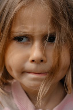 Uzun saçlı ve kahverengi gözlü küçük bir kızın portresini yakından çek. Kızgın ve hoşnutsuz bir çocuk. Doğada dinleniyor. Bulanık.