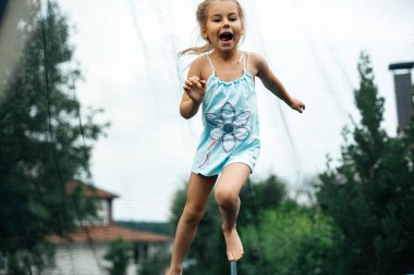  Yazın kulübede küçük bir kız trambolinde mutlu ve neşeli bir şekilde zıplıyor. Köyde çocuklar oynar. Temiz havada rahatla. Arkadaşlar trambolinde zıplar. Mutlu çocuk. Uzayı kopyala Tonlama.
