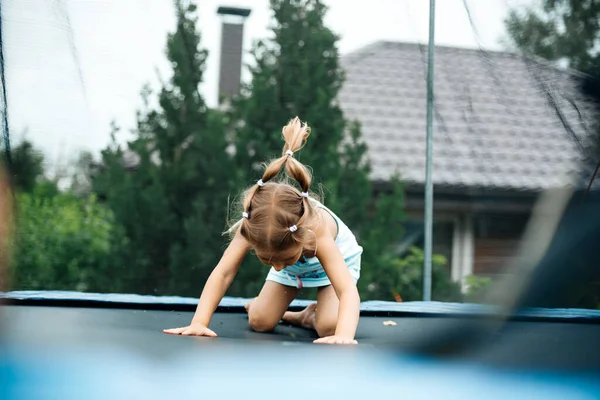 Little girl in the summer at the cottage jumps on a trampoline happy and joyful. Children play in the country. Relax in the fresh air. Friends jump on a trampoline.Happy child. Copy space. Toning.