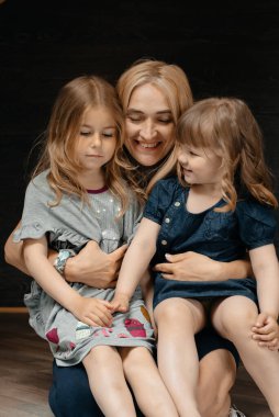 Genç ve çekici bir anne ve iki güzel kızı kucaklaşarak annelerinin kucağında oturuyorlar. Çocuk stili ve moda kavramı. Yaz tatili. Tasasız çocukluk. Tonlama.