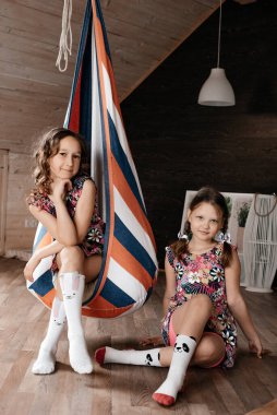 Çocuklar odada bir hamakta oturur, oynar ve konuşurlar. Kahverengi gözlü. Çocuk stili ve moda kavramı. Yaz tatili. Tasasız çocukluk. Tonlama.