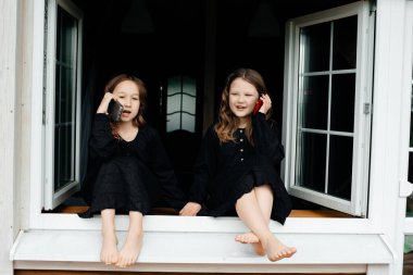 Siyah elbiseli küçük kızlar pencerede oturup telefonda konuşuyor, gülüyor ve gülümsüyorlar. Uzun parlak siyah saçlar. Yaz tatili Tasasız çocukluk. 