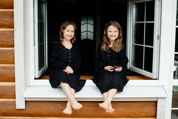 Siyah Elbiseli Küçük Kızlar Pencerede Oturup Telefonda Konuşuyor Gülüyor Gülümsüyorlar — Stok fotoğraf