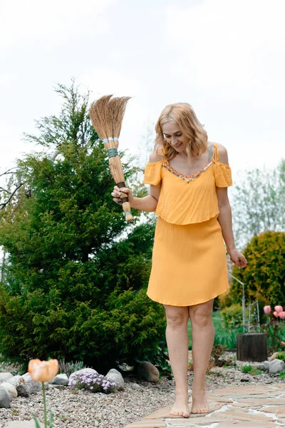 乡间一个穿着黄色浅色连衣裙的女孩手里拿着一把扫帚 自然与新鲜空气 — 图库照片